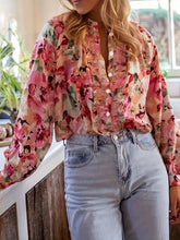 A woman wearing a long-sleeved floral print frill trim shirt in pink and peach shades on a light background