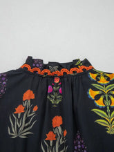 Black short sleeve shirt with frilled v neck, vibrant orange purple yellow floral embroidery, and bright orange crocheted neckline
