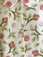 A cream-colored floral print blouse with pink roses green leaves classic white buttons and a peter pan collar