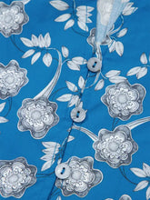 Blue hawaiian shirt with white and gray floral pattern and mother of pearl buttons in a floral print ruffle sleeve blouse style