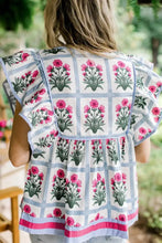A woman wears a floral print ruffle sleeve blouse with pink and green floral grid patterns and light blue trim