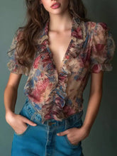 A floral print ruffle trim blouse in sheer fabric with pastel tones features ruffled detailing and puff sleeves