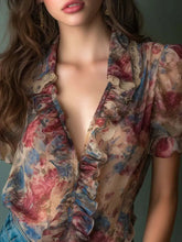 Sheer floral print ruffle trim blouse features ruffled edges and puff sleeves in soft reds blues and beige tones