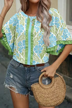 A woven straw handbag with a rounded half-moon shape and braided handle complements a ruffled color block blouse
