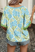 A woman wears a light blue and green floral print blouse that features ruffled color block trim half sleeves