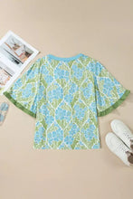 A light blue and green floral print short-sleeved blouse that features ruffled color block trim and ruffled cuffs