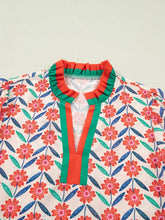 A cream floral print ruffled short sleeve blouse with bold red flowers blue green leaves and a striped ruffled collar