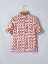 A vibrant coral and teal floral print ruffled short sleeve blouse with high collar displayed on wooden hanger