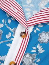Blue short sleeve blouse with white floral embroidery, red and white striped trim button neck, and tortoiseshell buttons