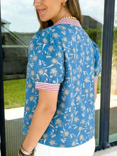 Blue floral print blouse featuring a striped trim button neck and cuffs with white and red accents short sleeve design