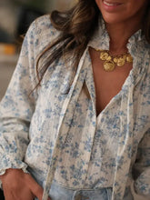 Ivory long sleeve blouse with subtle blue floral print and ruffled sleeves featuring a tie neck design