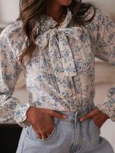 Ivory long sleeve blouse with subtle blue floral pattern and elegant tie neck bow at the neckline
