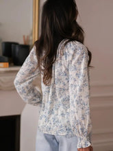 Delicate white long sleeve blouse with subtle blue floral pattern and gathered tie neck detailing