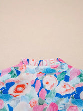 A floral print tie v neck blouse with ruffle short sleeves featuring bold pink blue and green blooms on light fabric