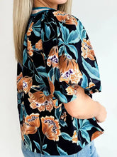 A black floral short bubble sleeve blouse with orange blossoms teal leaves and a notched neck in a flowing silhouette