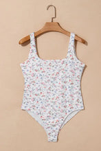 White one-piece swimsuit with delicate pink and blue floral pattern featuring a floral textured square neck sleeveless design