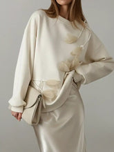 Cream-colored satin skirt with a sleek flowing silhouette paired with a flower dropped shoulder sweatshirt