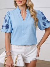 Light blue textured blouse with navy flower embroidered puff sleeves and a split neck design
