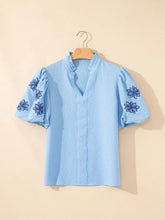 Light blue textured blouse with flower embroidered puff sleeves and dark blue floral embroidery on the shoulders