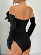 Black off-the-shoulder long sleeve bodysuit with large ruffled flower embellishment on the left shoulder long design
