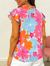 A flower printed sleeveless blouse with neck ruffle and bold pink and blue floral design on white background