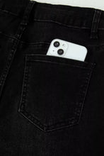 A white iphone peeks from the back pocket of black denim frayed cropped straight jeans showing the back side