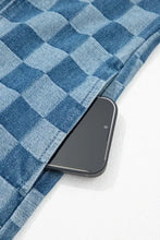 A black smartphone rests in the pocket of a blue frayed hem checkered denim mini dress