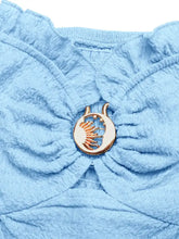 Gold-toned crescent moon pin with stars and handprint on the ruffled neckline of a light blue frill tube top with buckle detail
