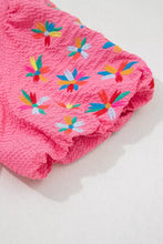 Pink textured shorts with colorful embroidered flowers paired with a frilled v neck flower embroidered puff sleeve blouse