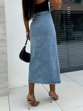 Light-wash midi denim skirt with front button slit and visible stitching along the straight cut seam