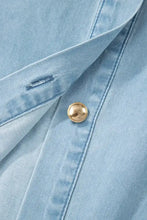 A gold-toned round button with textured edge on light blue denim fabric of a buttons collared short bubble sleeve dress