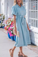 A light blue denim dress with full buttons collared short bubble sleeves and a belted waist midi length
