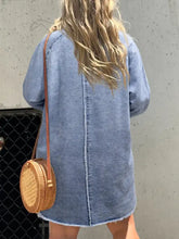 A round woven wicker crossbody bag with tan leather strap styled with a full size button-front denim shirt dress