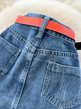 A vibrant orange leather belt with white stitching fastened around the waist of a full size striped patchwork denim skirt
