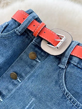 A vibrant orange leather belt with silver buckle fastened around blue denim jeans featuring a striped patchwork denim skirt