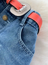 A vibrant orange leather belt with silver buckle fastened on striped patchwork denim skirt plus size waistband