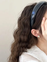 Glossy leather wide headband in wavy brown hair with pearl earring