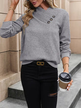 Gray textured sweater with asymmetrical neck, buttons, and black distressed jeans