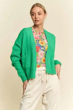 Green drop shoulder cardigan with relaxed fit over floral shirt and white pants