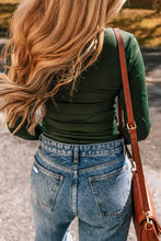 Green long sleeve bodysuit with high-waisted jeans and brown leather saddlebag