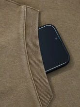 A black smartphone rests partially in the ribbed seam of a tan mineral wash baggy half zip kangaroo pocket hoodie