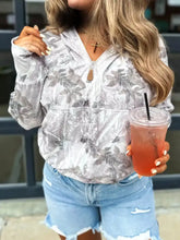 A woman wears a light gray half-zip long sleeve hoodie with a subtle leaf pattern and brown zipper pull, slightly stretchy and machine wash cold