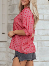 A pink heart print button-down shirt with subtle textured weave and scattered red heart print worn by a woman