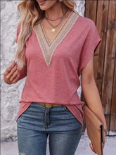 Woman in heathered short sleeve V-neck T-shirt with cream lace trim, jeans, tan clutch