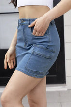 High waist pocketed denim skirt in medium blue wash with two large cargo pockets and button closure mid-thigh length