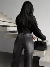Black handbag with structured design and smooth material next to high-waisted slit hem jeans
