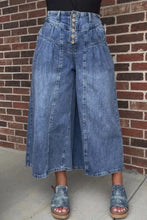 High-waisted wide leg button-fly jeans in medium blue denim with pleated front panels and button closures