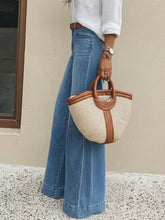 Beige woven straw tote bag with brown leather handles and trim paired with slightly stretchy high-waisted wide leg jeans