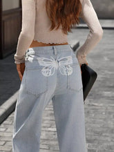 Back side of high waisted wide leg light-wash denim jeans with a white butterfly design on the back pocket