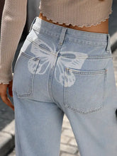 Back side of high waisted wide leg light-wash denim jeans with a white butterfly graphic on the back pocket